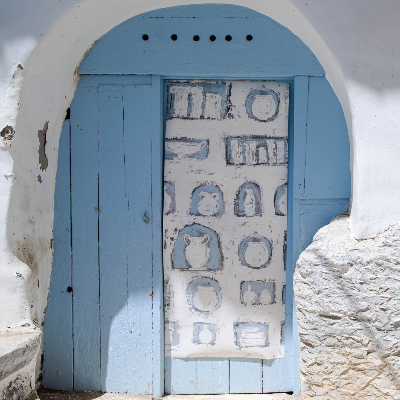 Blue door with wallpaper with decorative patterns in a white-washed wall