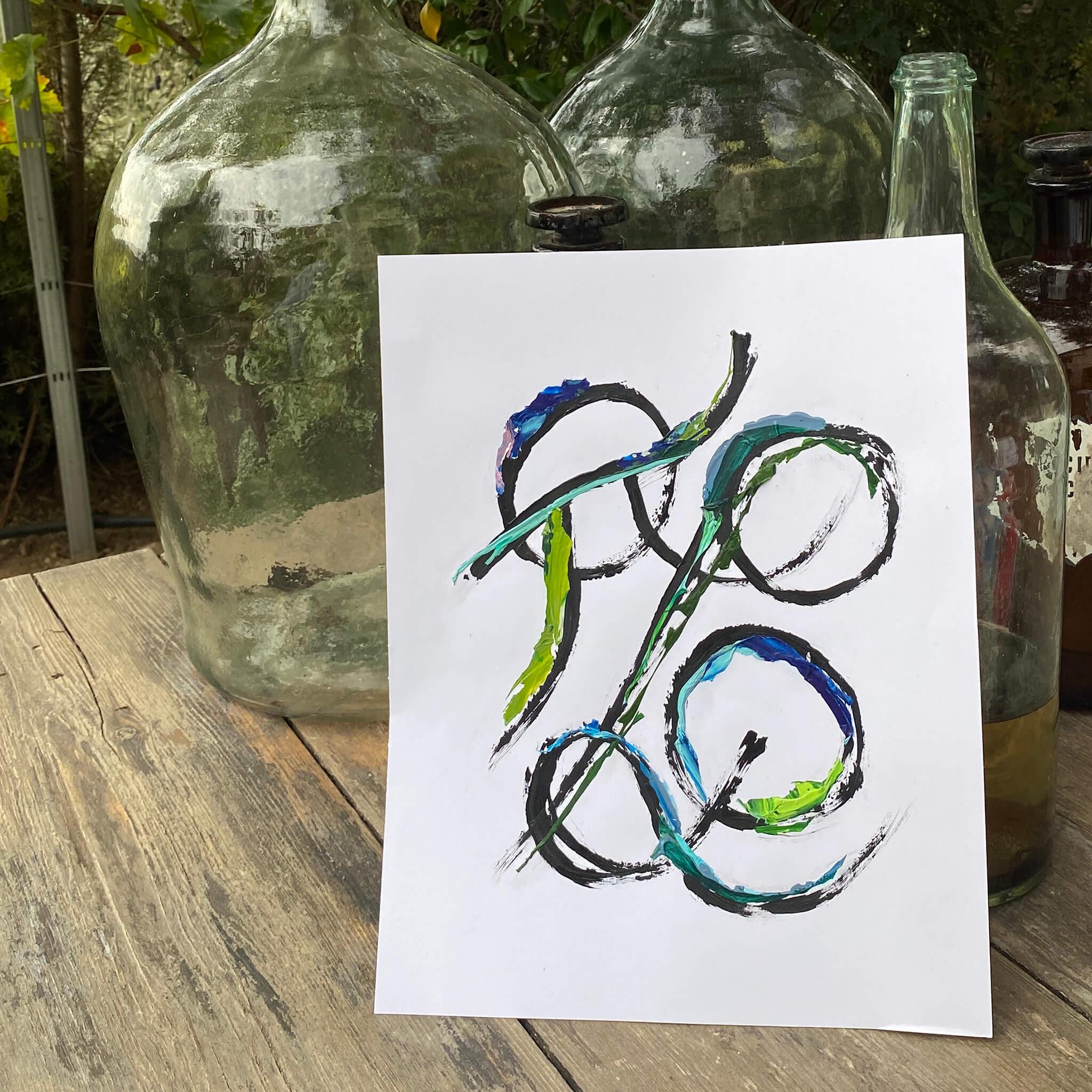 Custom Grammata multicolor painting by Richmond artist Theodora Miller, featuring intertwined Greek initials in black acrylic with blue and green recycled paint skins, styled on a rustic wood table with vintage glass bottles.