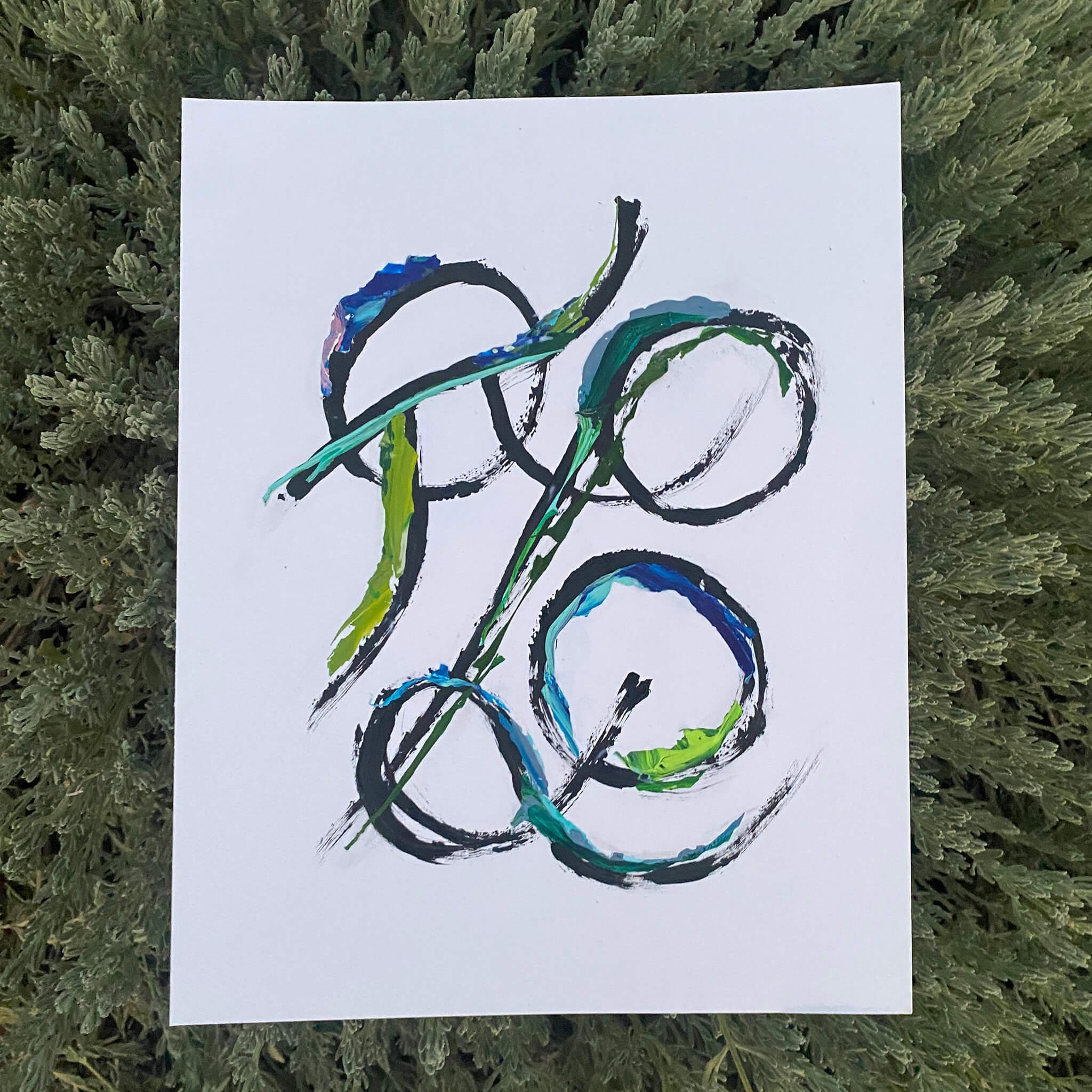 Custom Grammata multicolor painting by Richmond artist Theodora Miller, featuring intertwined Greek initials in black acrylic with blue and green recycled paint skins, photographed against textured greenery.