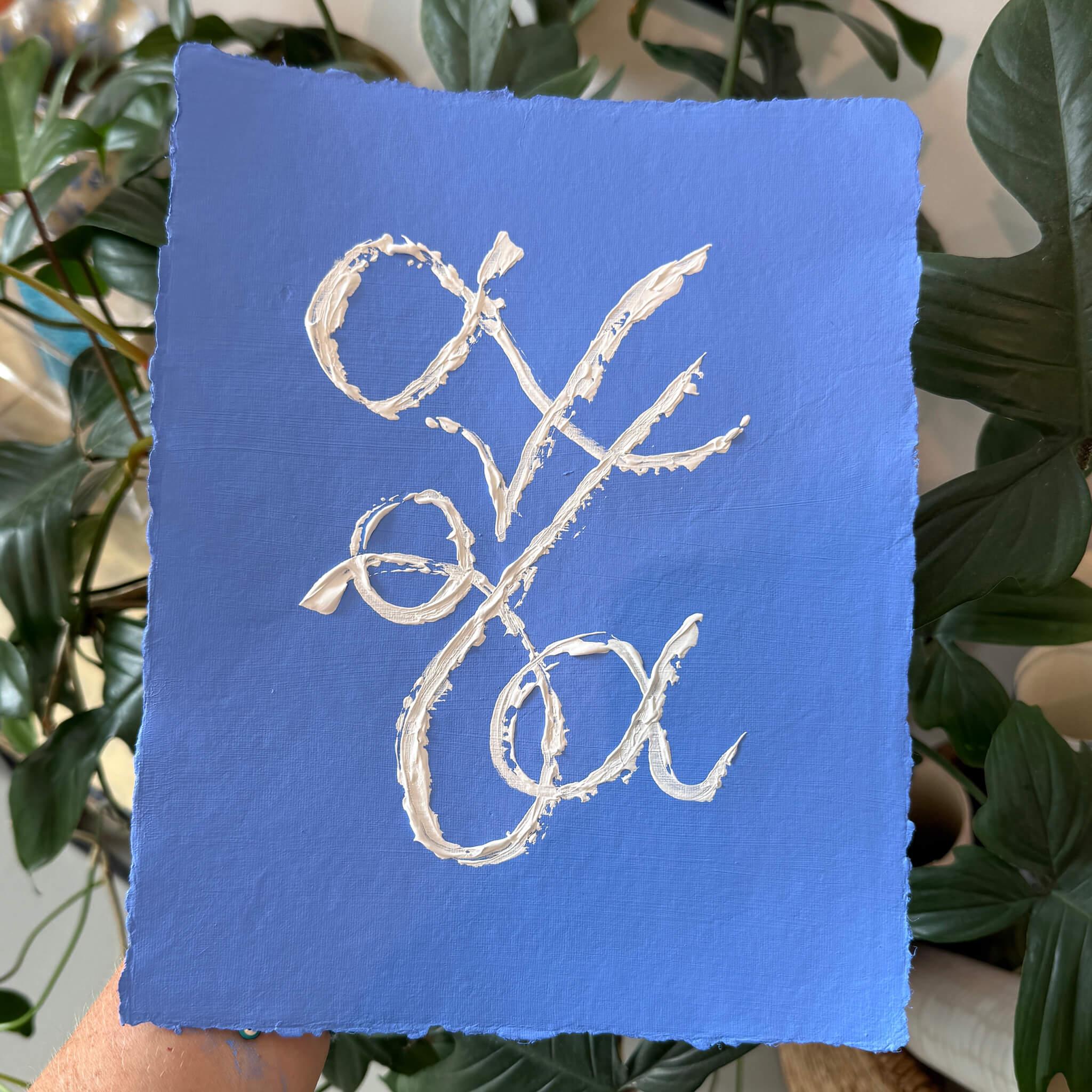 Blue handmade paper with white cursive text painted, held by a person against a green leafy background